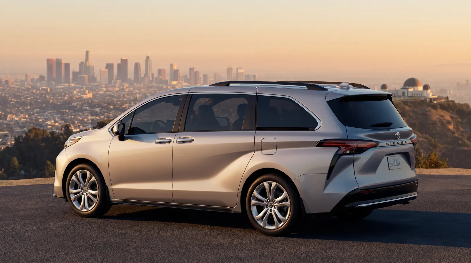 Silver minivan parked at a hilltop overlook above the Los Angeles skyline at golden hour